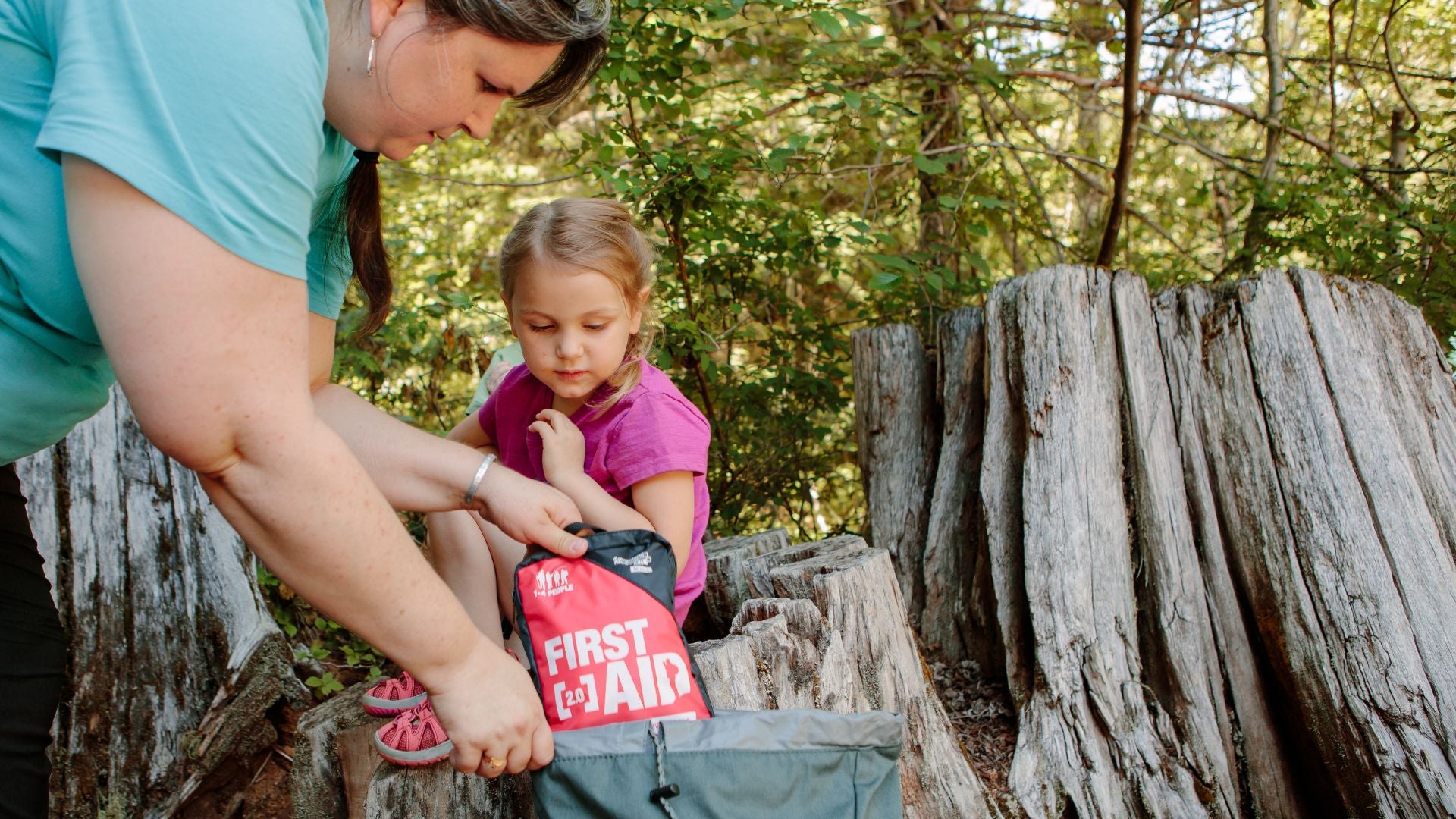 Mom hiking with daughter taking medical kit out of backpack