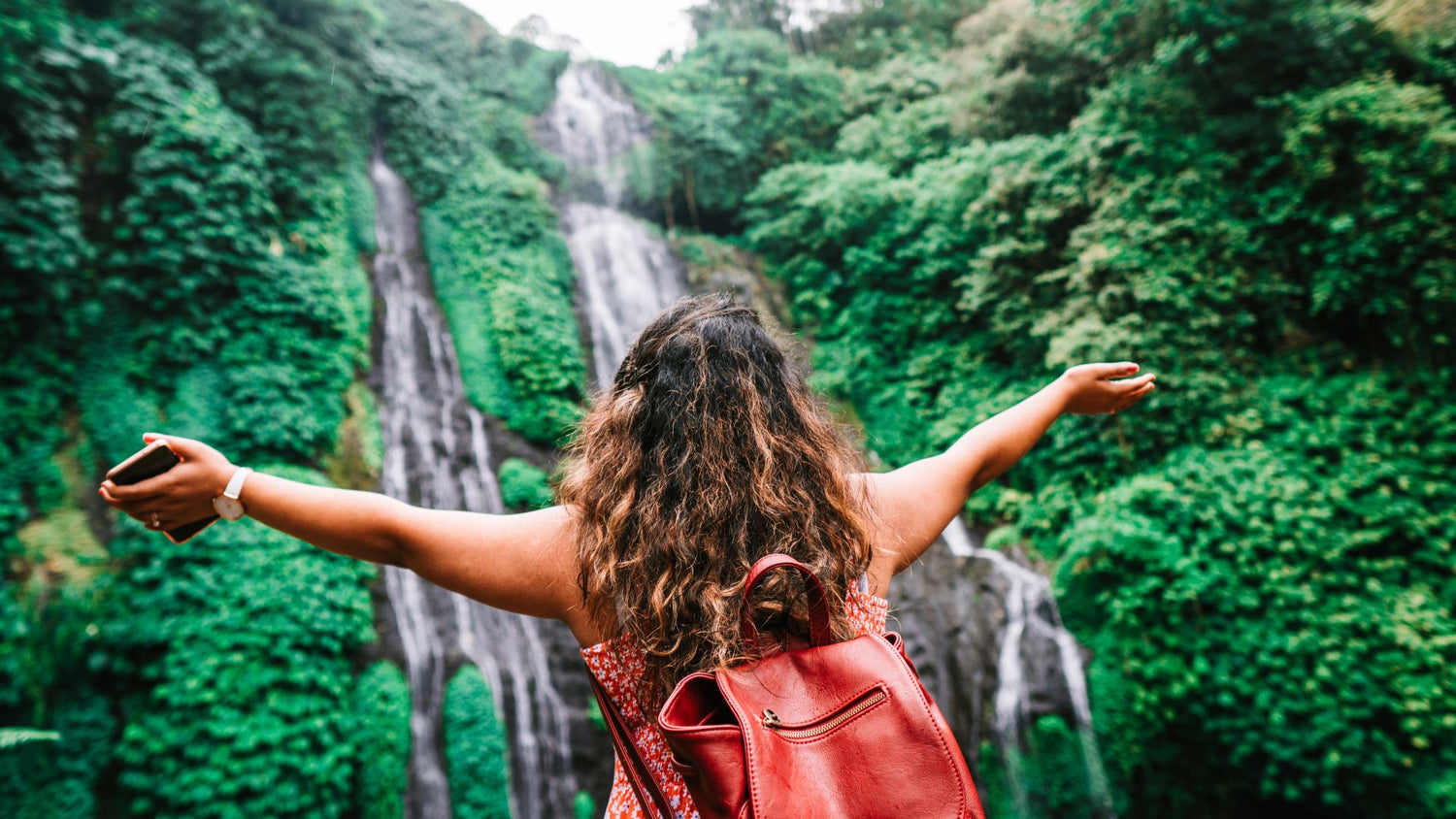 Woman standing in front of waterfall with arms outstretched