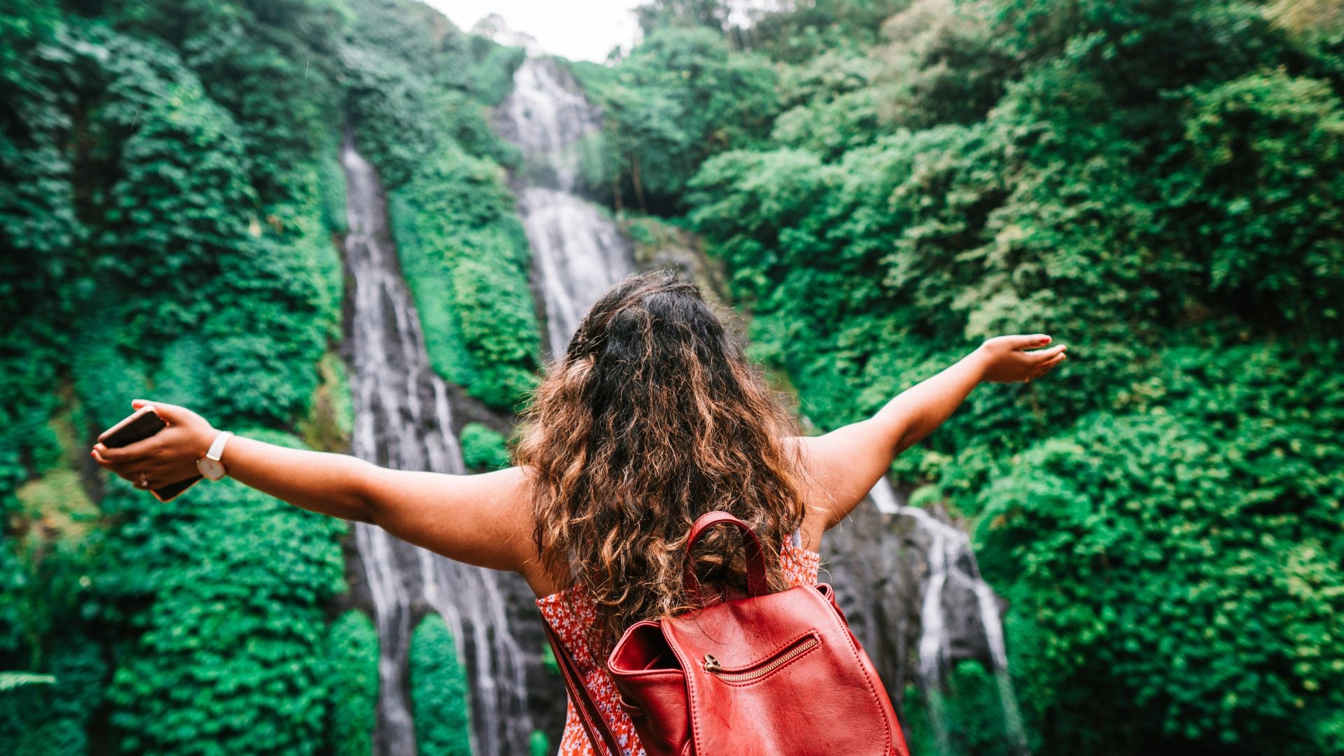 Woman standing in front of waterfall with arms outstretched