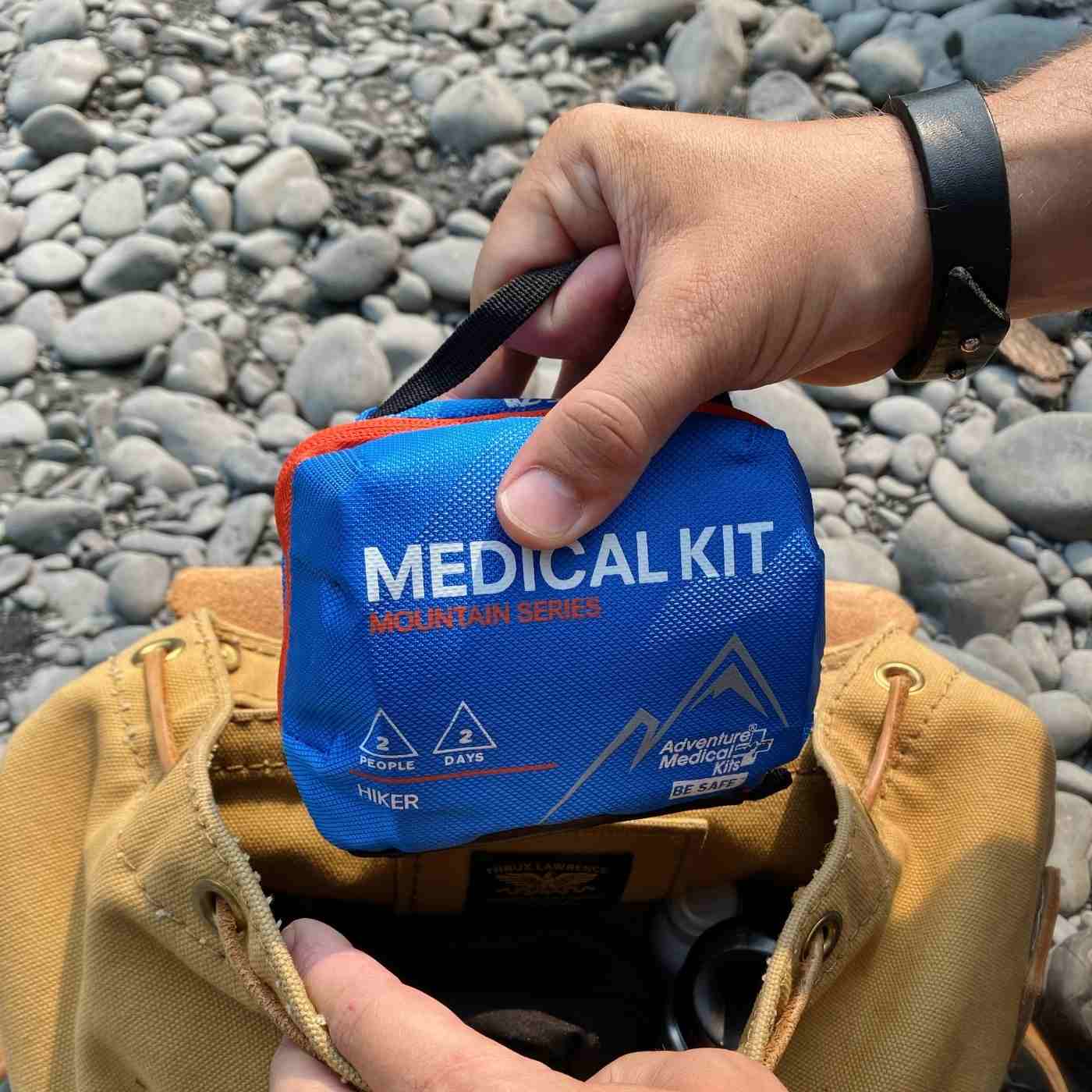 Mountain Series Medical Kit - Hiker pulling kit out of brown bag on rocky ground