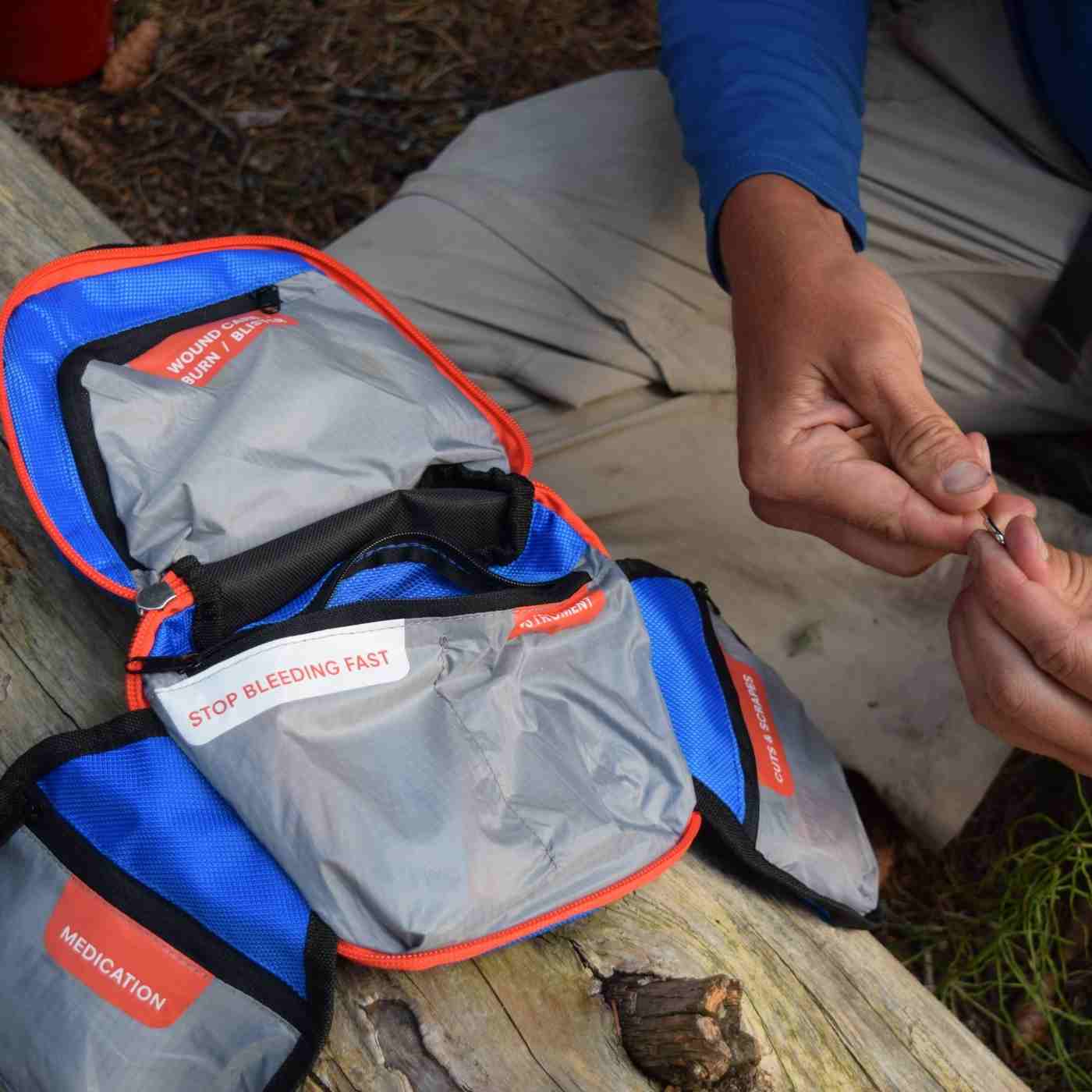 Mountain Series Medical Kit - Backpacker kit opened with man using tweezers on log