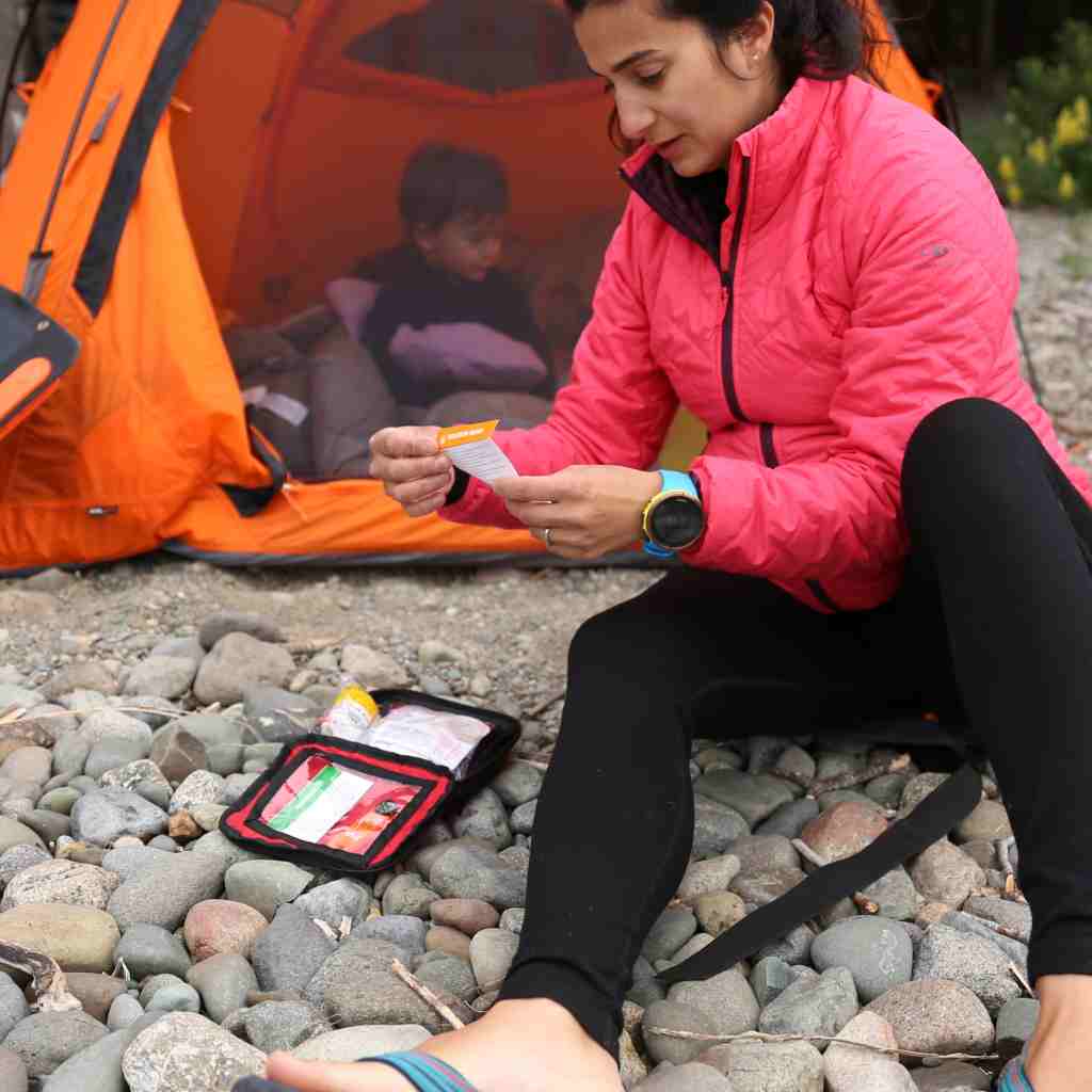 Adventure First Aid, 1.0 woman using kit in front of orange tent with child inside