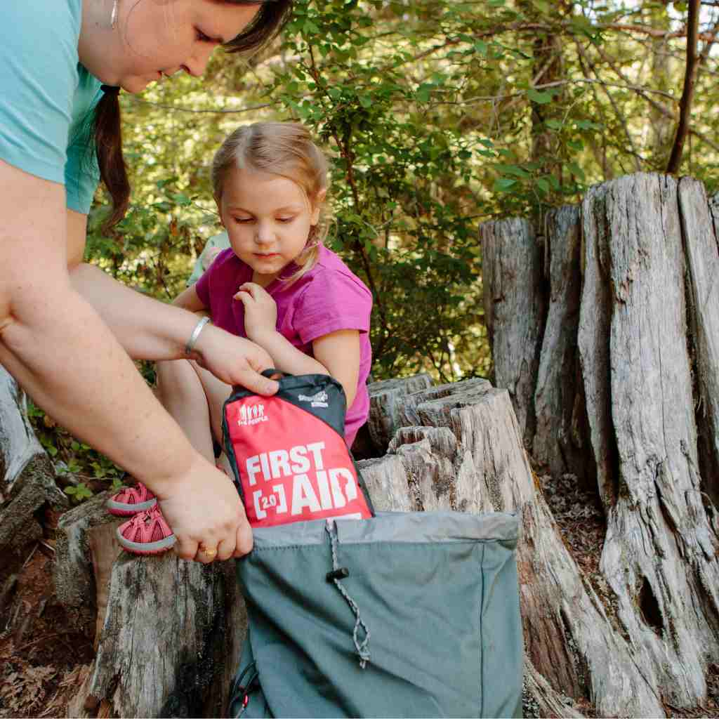 Adventure First Aid, 2.0 woman pulling kit from backpack next to child