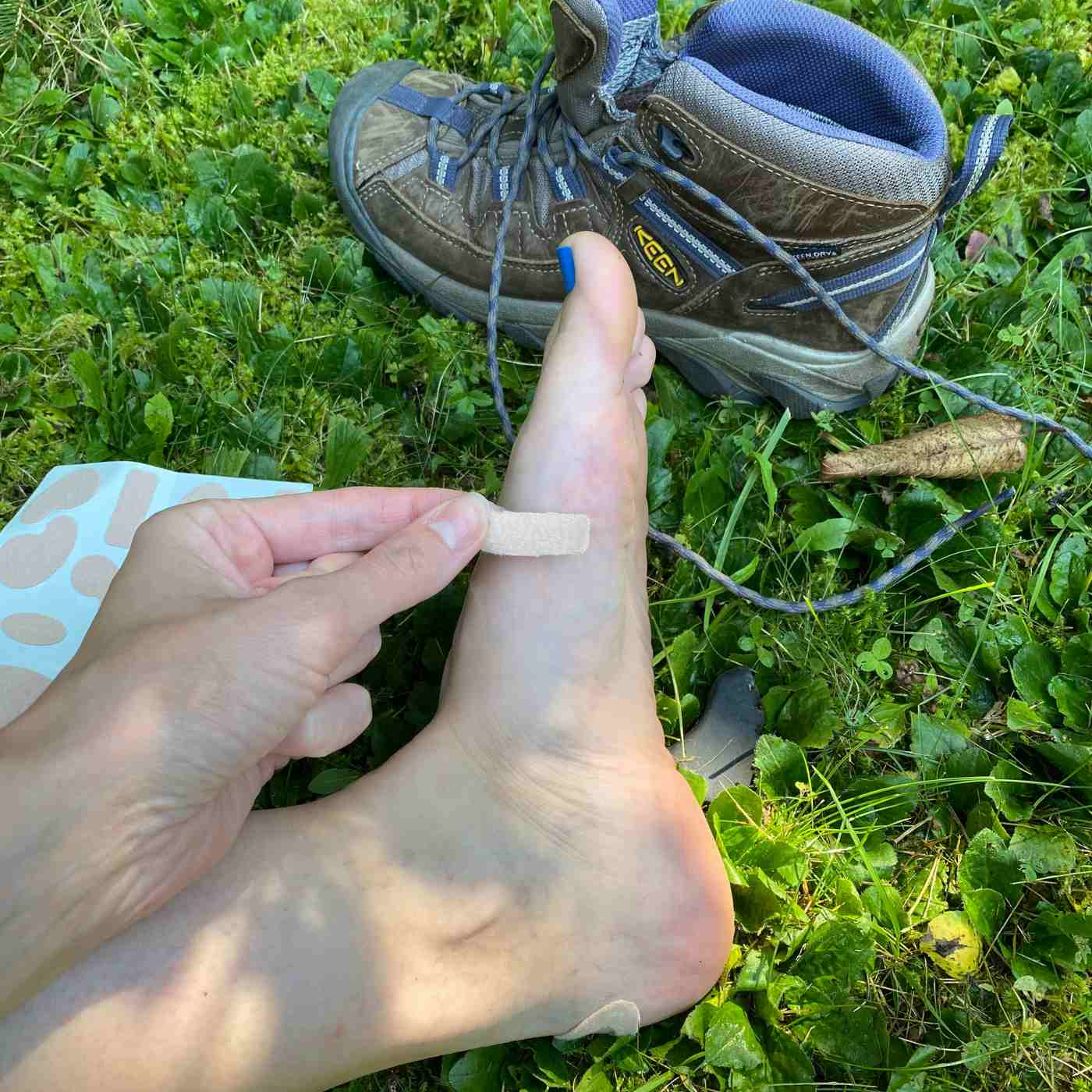 Moleskin Pre-Cut and Shaped applying to side of foot while seated next to shoe on grass