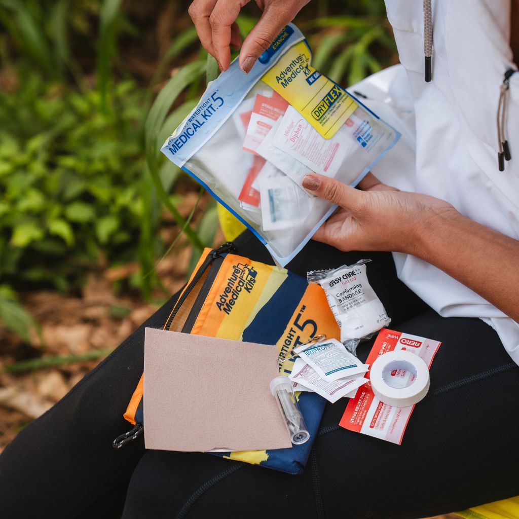 Person holding a medical kit with various supplies outdoors