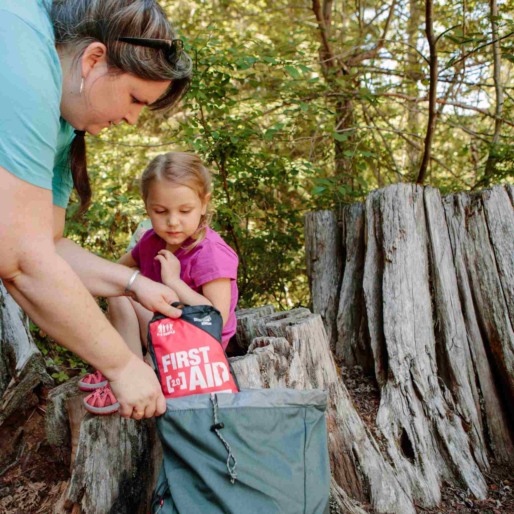 Adventure First Aid, 2.0 woman pulling kit from backpack next to child