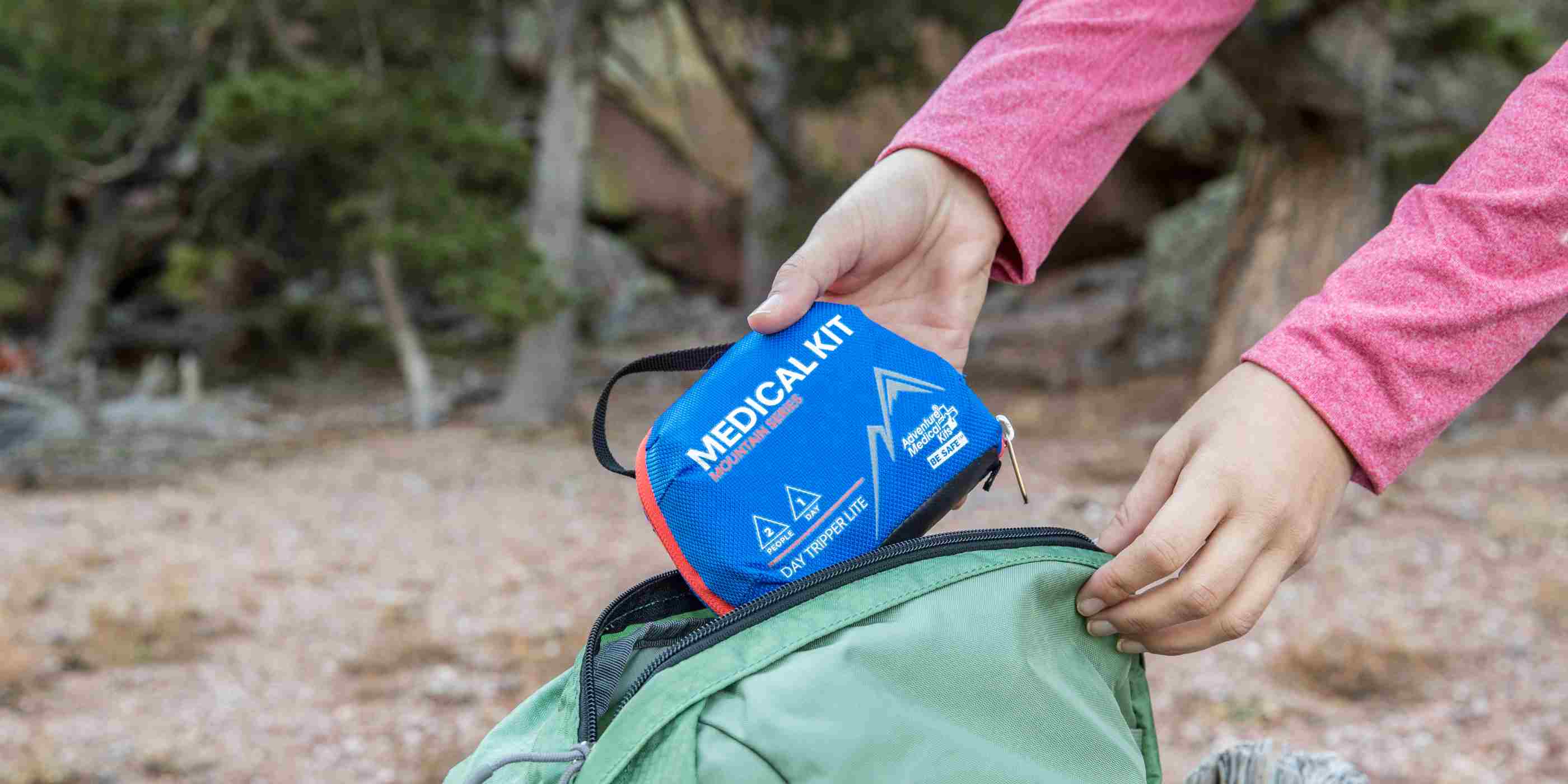Mountain Series Medical Kit - Day Tripper Lite woman pulling kit from green backpack