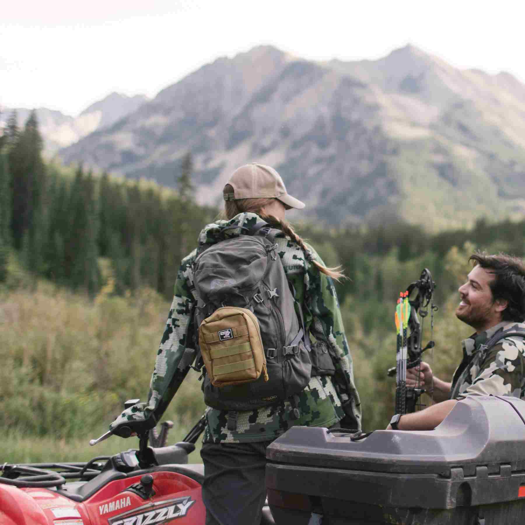 MOLLE Bag Trauma Kit 2.0 - Khaki kit attached to backpack of woman in camo on ATV next to man with bow and arrow