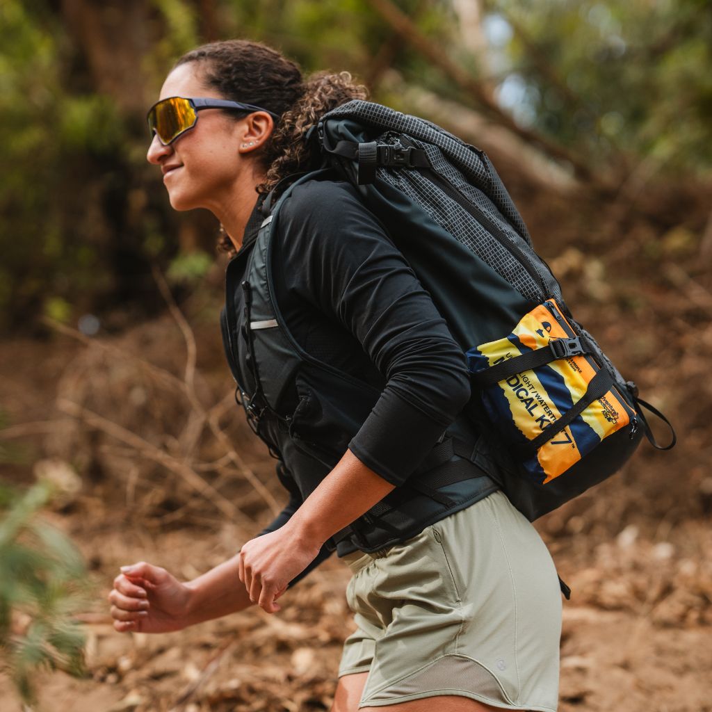 Person hiking with a backpack in a forest and a medical kit strapped to their pack