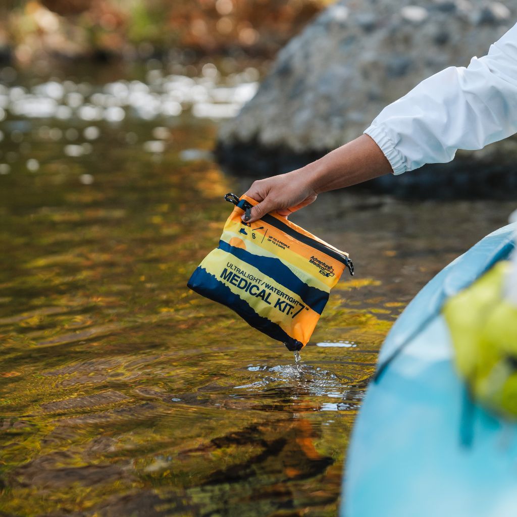 Person holding a waterproof medical kit above a body of water
