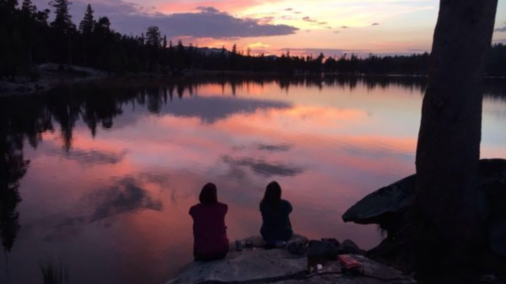 lake at sunset with two people sitting on rock looking out