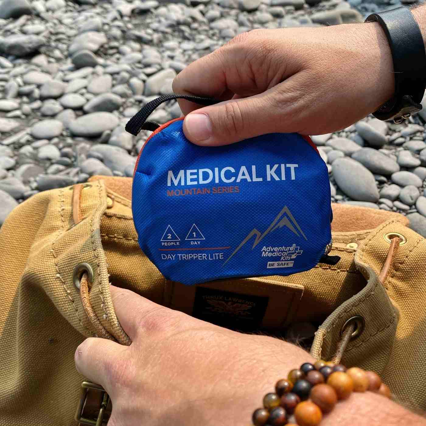Mountain Series Medical Kit - Day Tripper Lite man pulling kit out of brown backpack on rocky ground