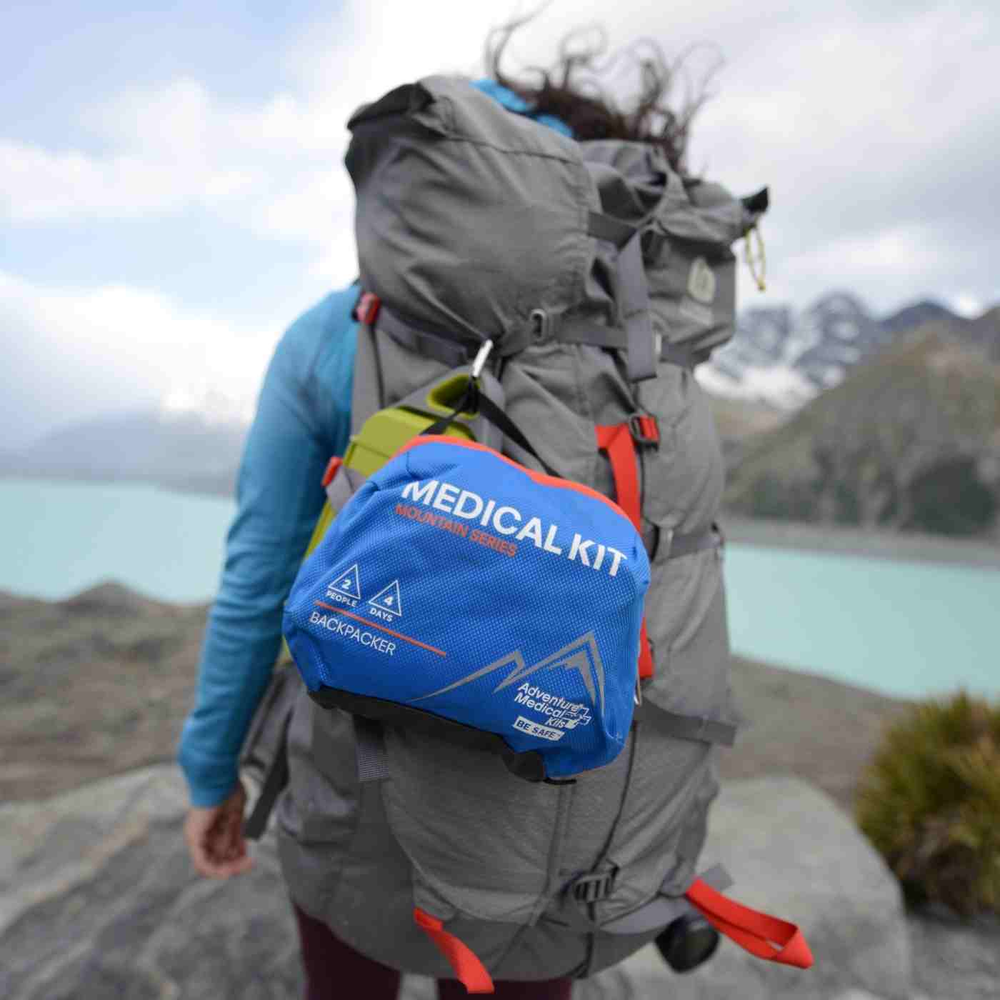 Mountain Series Medical Kit - Backpacker on woman's gray backpack while hiking in front of lake