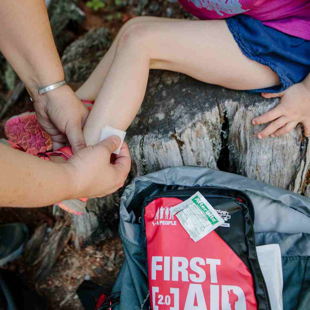 Adventure First Aid, 2.0 applying After Bite wipe to child's leg next to kit