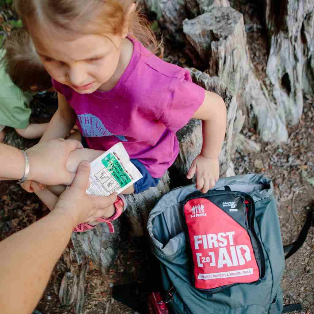 Adventure First Aid, 2.0 woman using cold pack on child next to kit and backpack