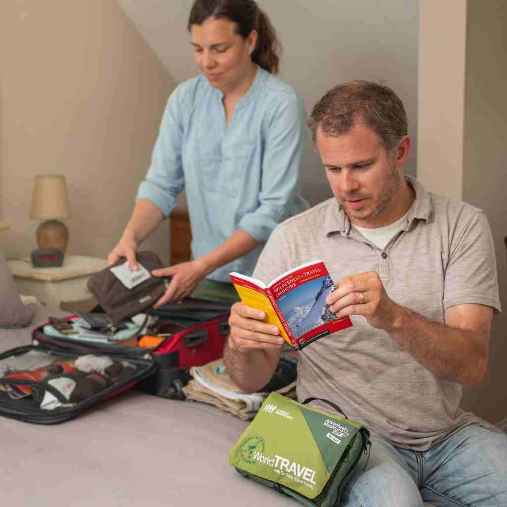 Travel Series Medical Kit - World Travel man reading book with kit in front of him with wife packing a bag