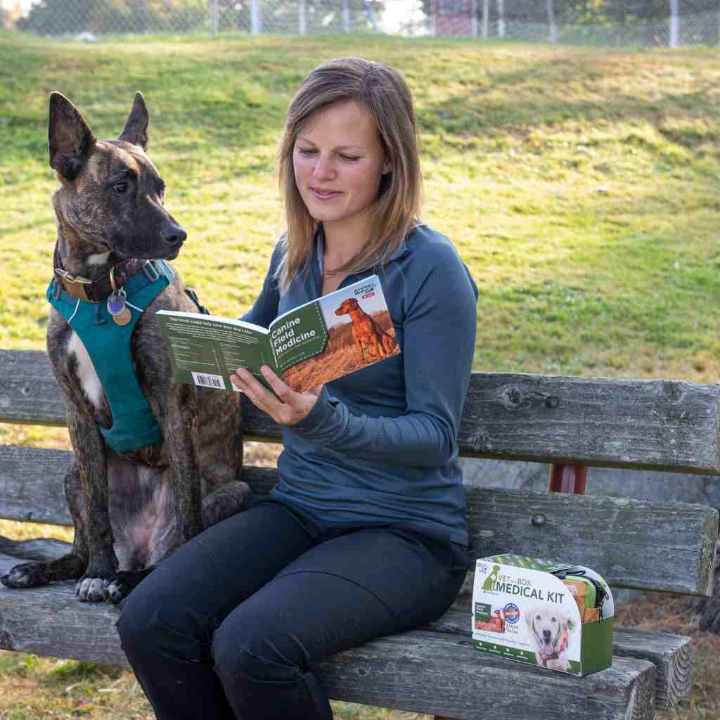 Adventure Dog Medical Kit - Vet in a Box woman reading Canine Field Medicine book seated next to dog on a bench with kit next to her