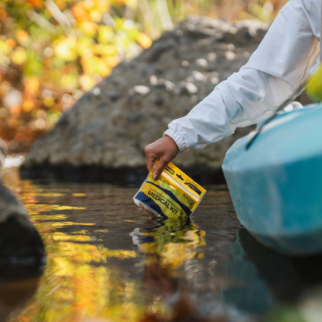 Person holding a medical kit over water with a kayak in the background