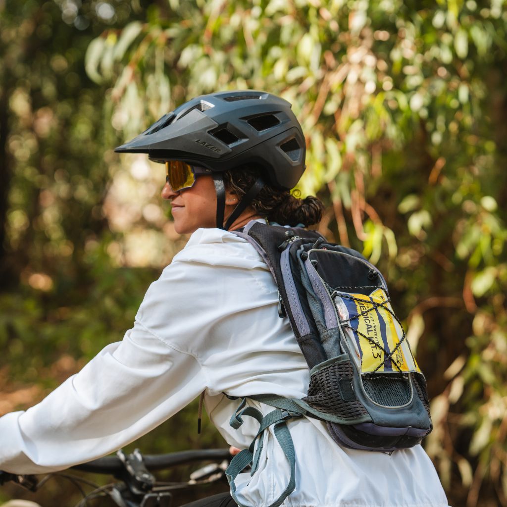 Person wearing a helmet and backpack, riding a bike with greenery in the background