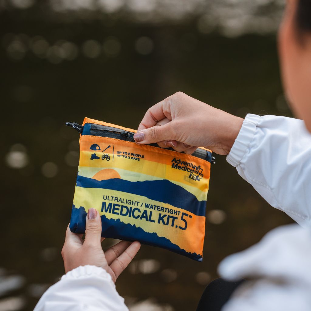Person holding an ultralight watertight medical kit with a blurred natural background