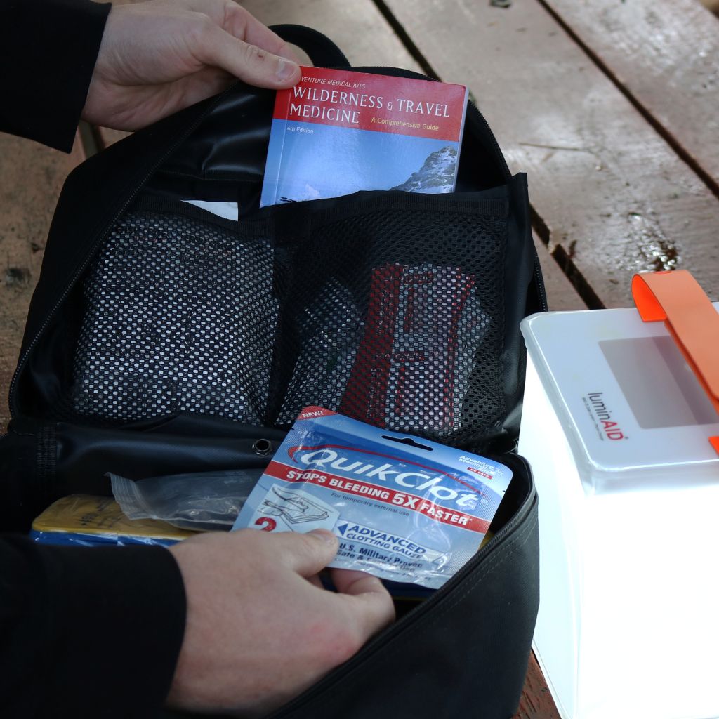 MOLLE Pro first aid kit with Wilderness & Travel Medicine and QuikClot bandages next to a solar lantern on a wooden surface.