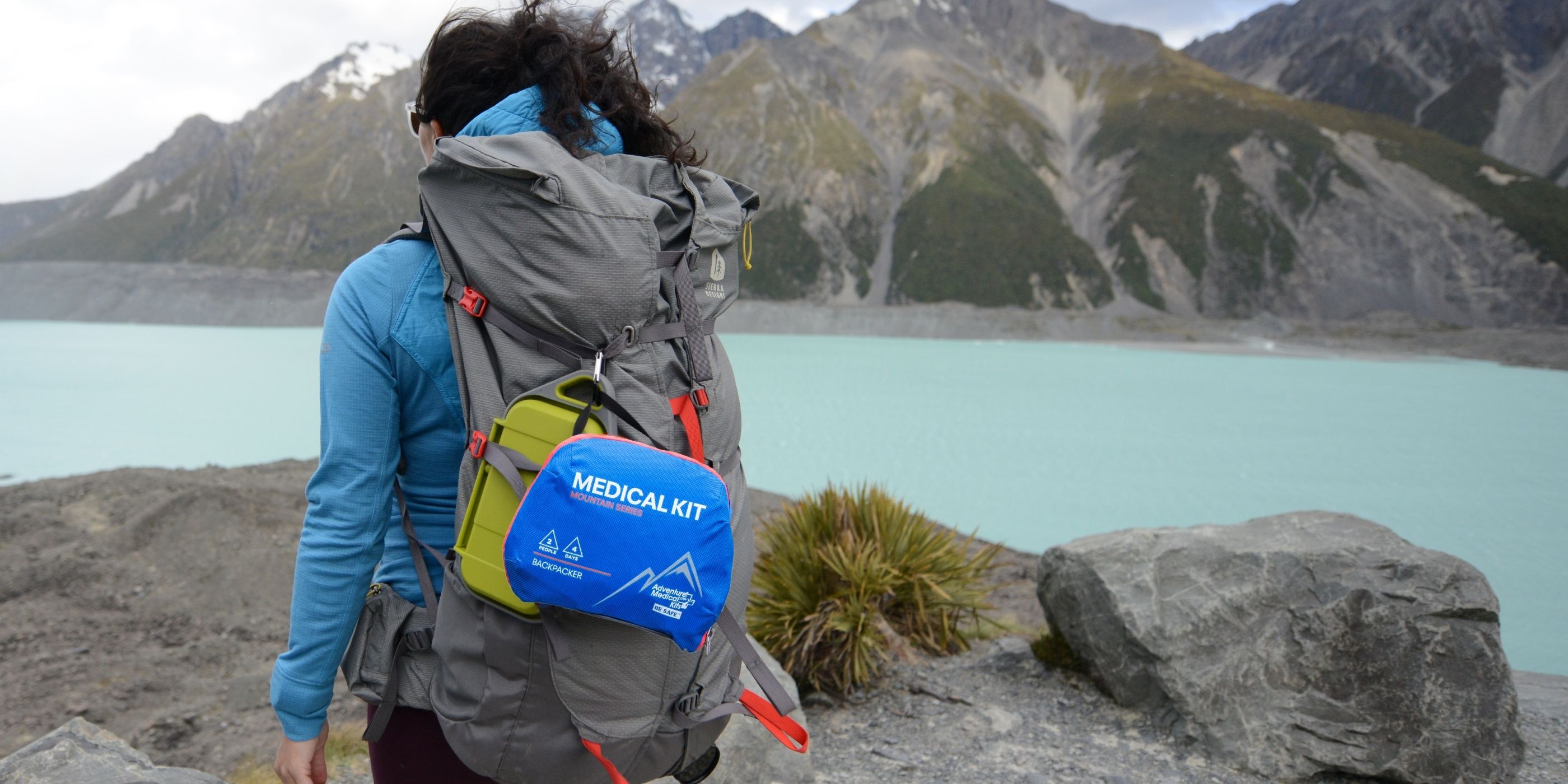 Woman hiking in front of lake with Adventure Medical Kits Backpacker Kit on her backpack