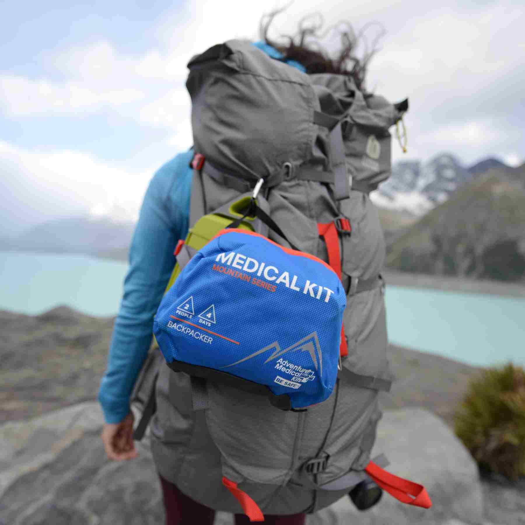 Mountain Series Medical Kit - Backpacker on woman's gray backpack while hiking in front of lake