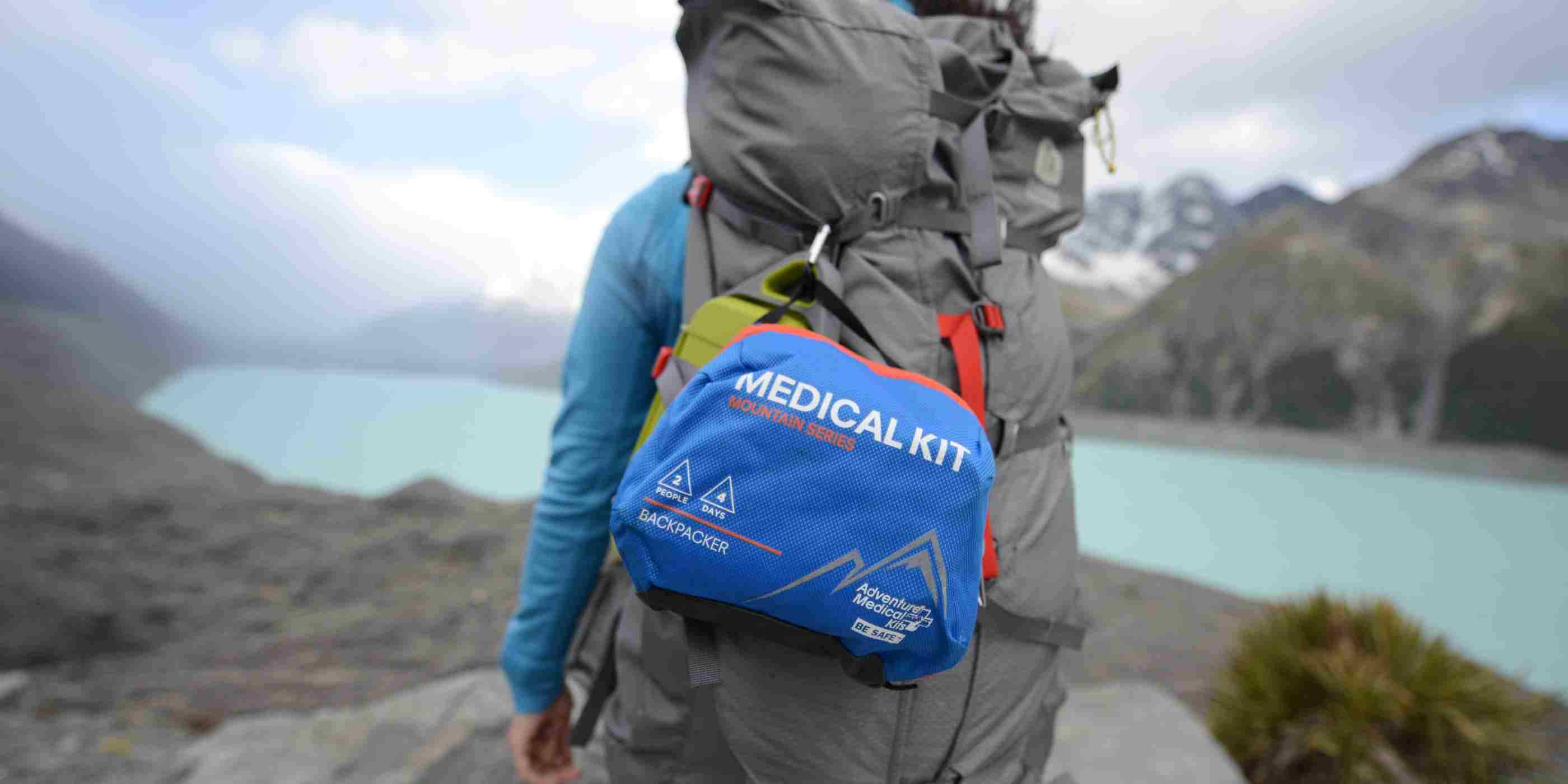 Mountain Series Medical Kit - Backpacker on woman's gray backpack while hiking in front of lake