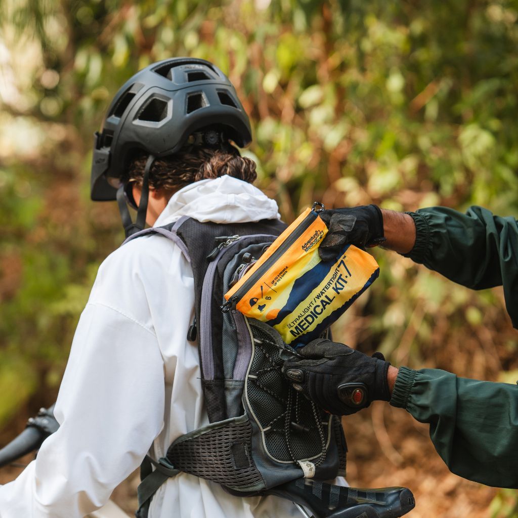 Person wearing a helmet and backpack with a medical kit, surrounded by greenery.