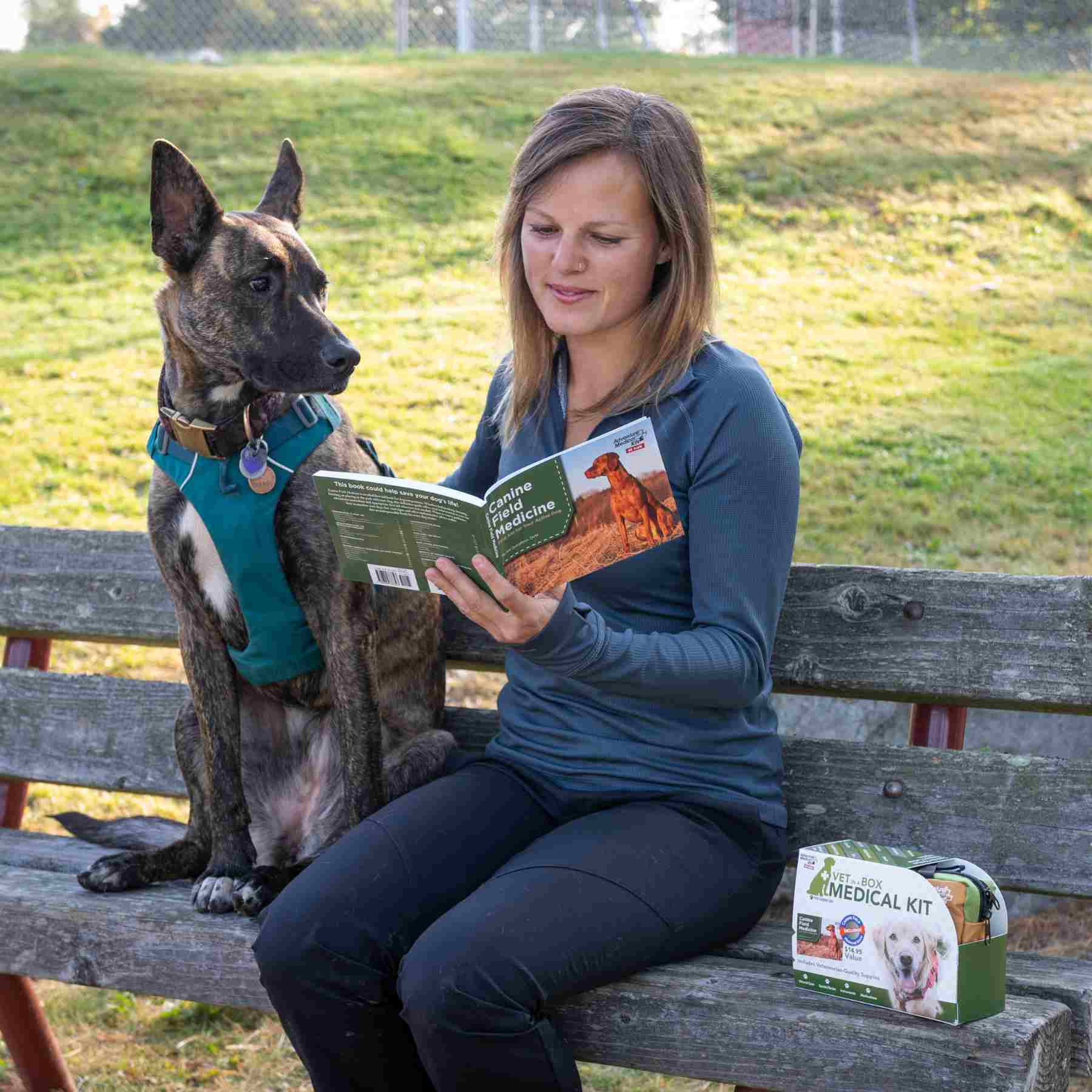 Adventure Dog Medical Kit - Vet in a Box woman reading Canine Field Medicine book seated next to dog on a bench with kit next to her